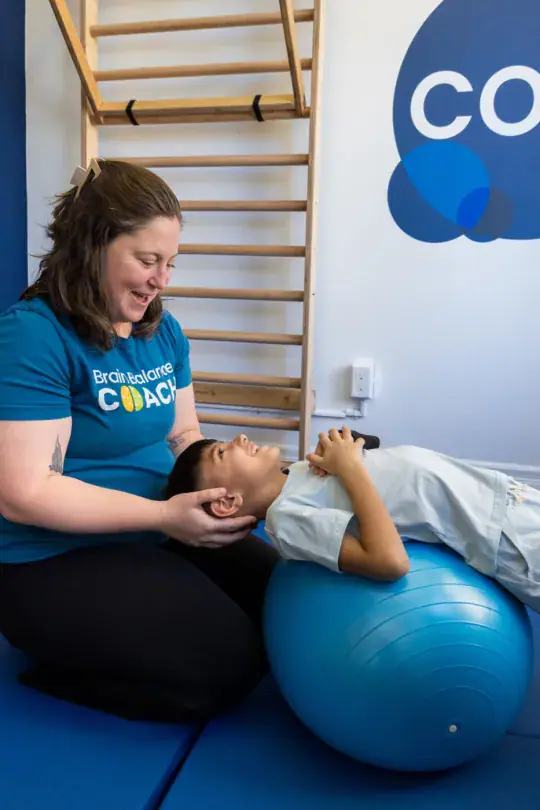 A coach kneeling beside a boy lying back over an exercise ball